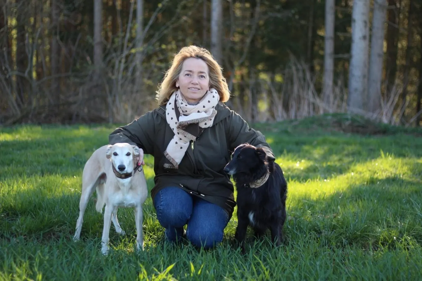 Jowita Meisner kniet mit zwei Hunden auf einer Wiese am Waldrand
